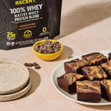 Scoop junto a bolsa Ascent indicando porción de 25 g de proteína por servicio