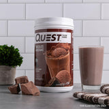Comparación de tamaño del envase Quest Chocolate Milkshake y cucharada medidora, práctico para porciones
